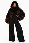 Model wearing a dark brown hooded faux-fur cape with voluminous sleeves.